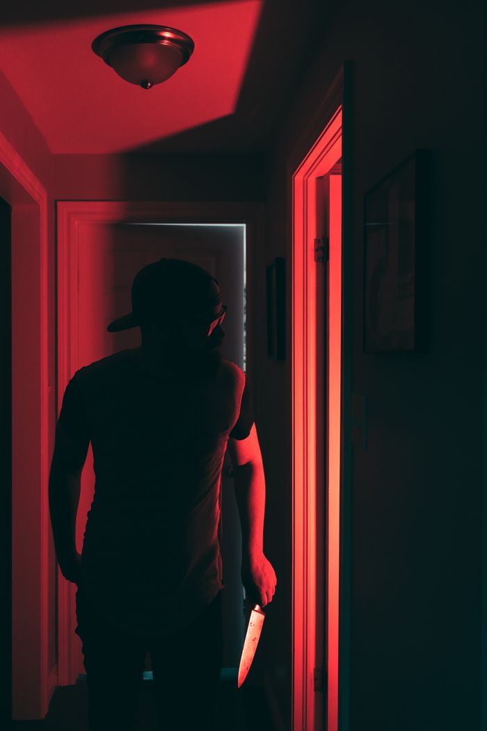 Silhouette of a figure holding a knife in a red-lit hallway, evoking suspense.