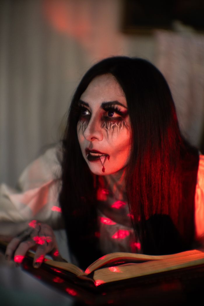 A mysterious woman with gothic makeup reading an old book on Halloween night.