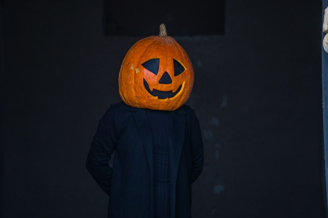 A person with a pumpkin head dressed in dark clothing, evoking a Halloween theme.