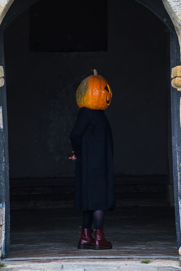 A mysterious figure with a pumpkin head stands in an arched doorway, creating a spooky Halloween vibe.