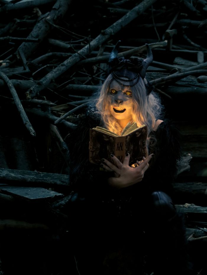 Eerie mystical figure with horns illuminated by a book in a dark forest setting, creating a mysterious atmosphere.